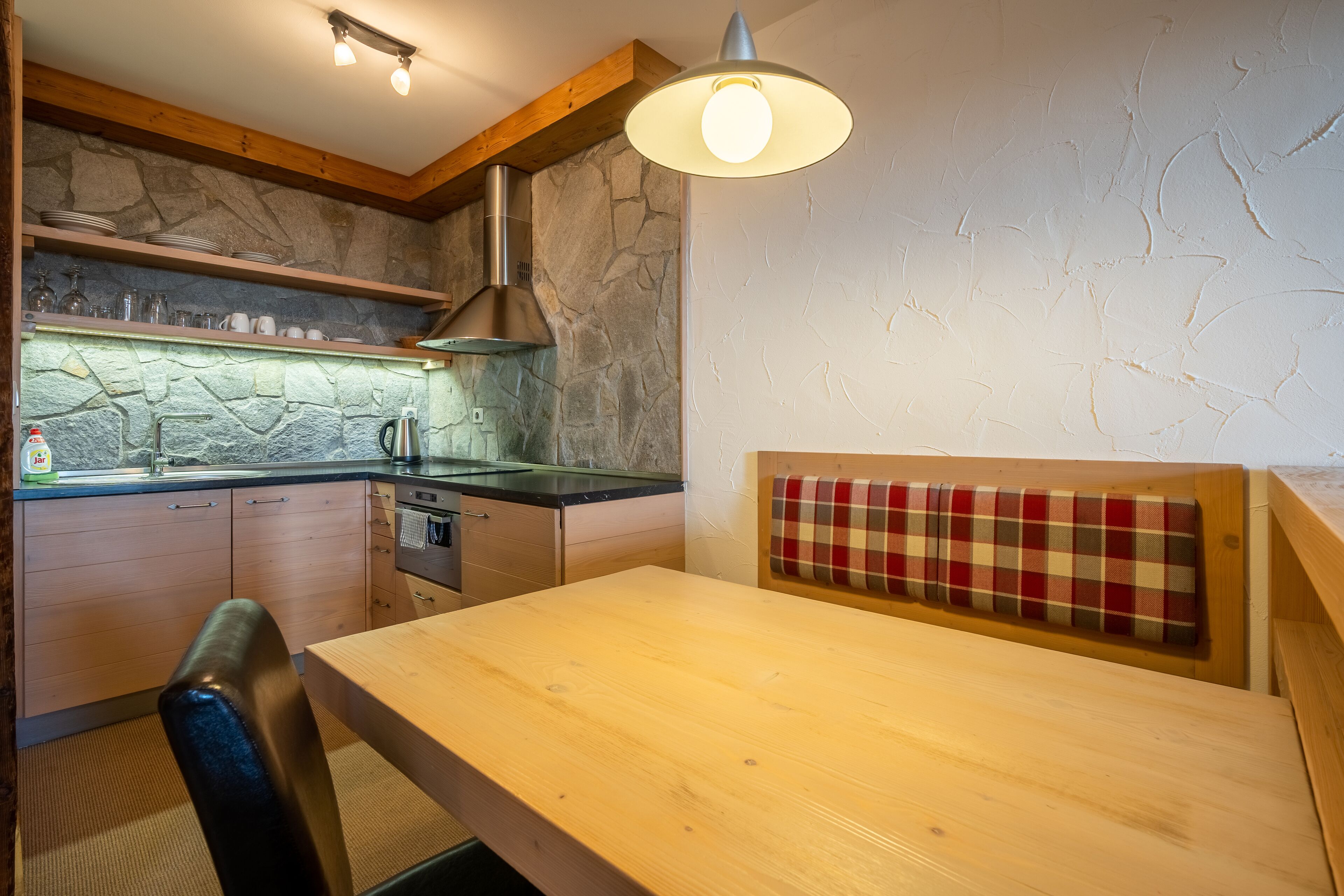 A cozy kitchen with a stone backsplash, wooden cabinets, a built-in stove, and a plaid-patterned bench.