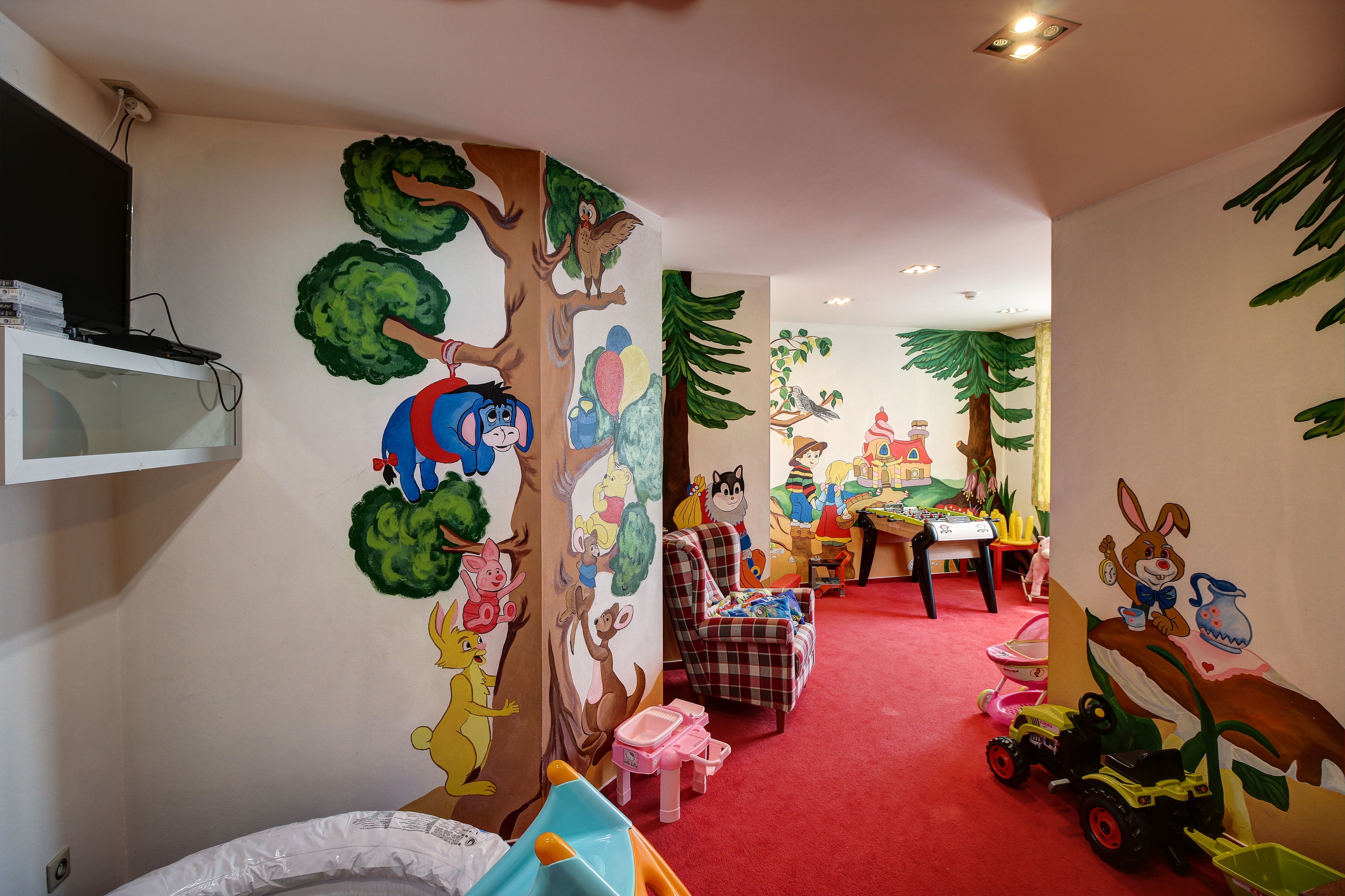 A child's playroom with colorful wall murals, a television, and various toys.