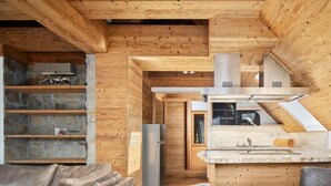 A cozy cabin interior with a wooden interior, a stone fireplace, a kitchen area, and a seating area with a sofa and a table.