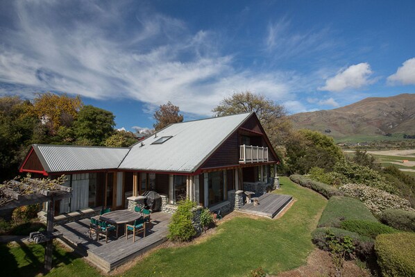 A house with a large deck, outdoor seating, and a scenic view of hills and trees. - Release Wanaka - Bullock Creek Chalet (Wanaka)