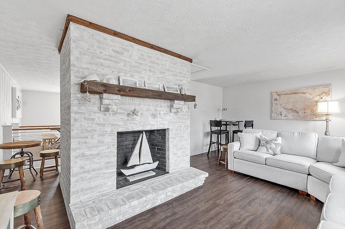 A living room with a white brick fireplace, a white sofa, and a dining area with wooden tables and chairs.