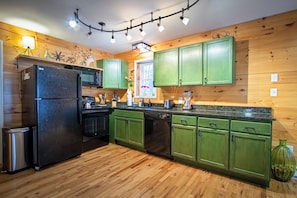 A kitchen with green cabinets, a black refrigerator, and a wooden floor.