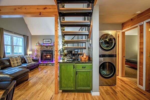 A modern living room with a fireplace, a staircase, and a laundry area.