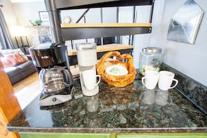 A kitchen counter with a coffee maker, cups, a basket, and jars.