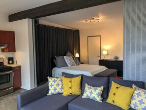 Una habitación de hotel moderna con cama, sofá, escritorio y zona de cocina.