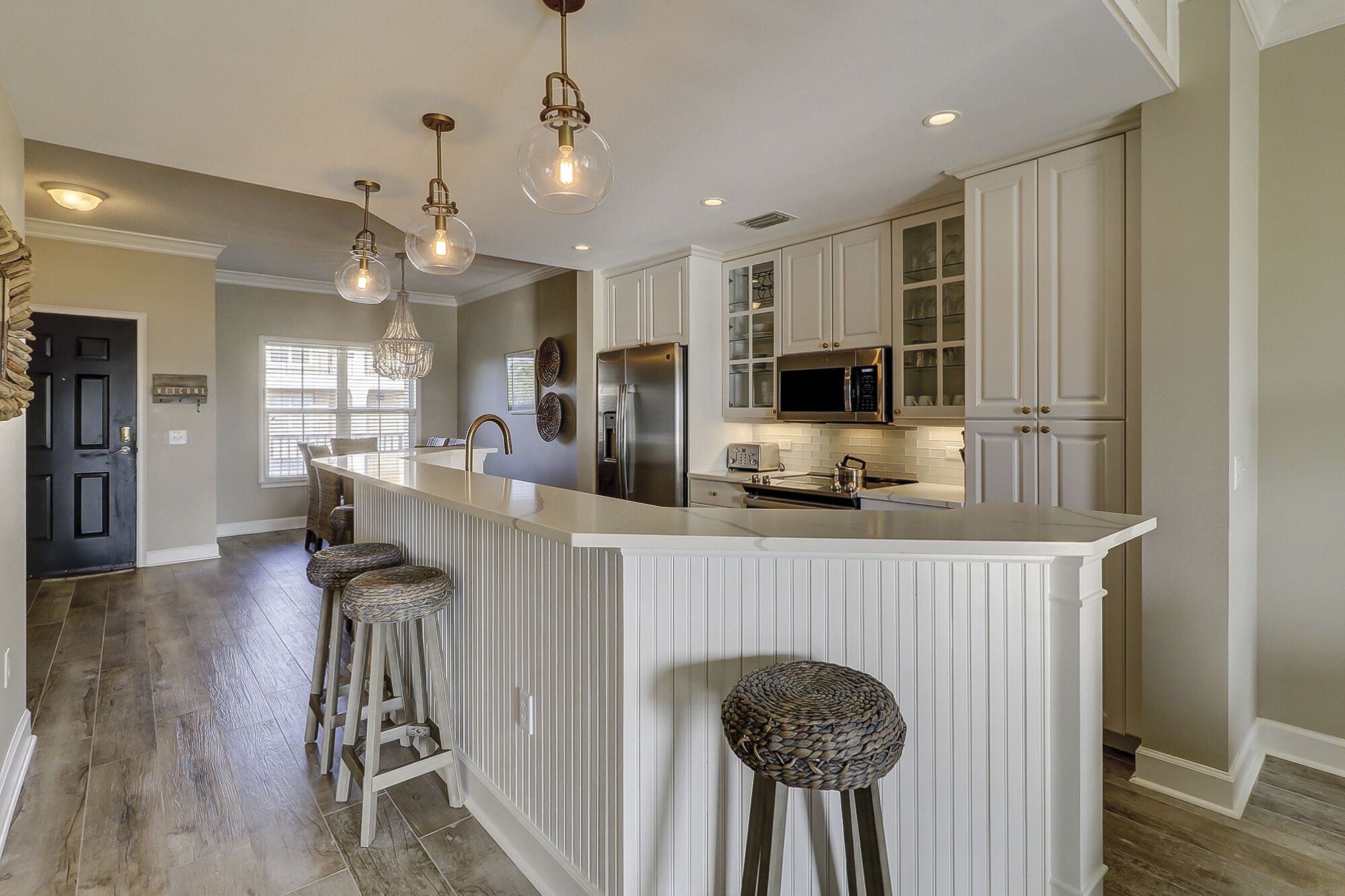 A modern kitchen with a central island, bar stools, stainless steel appliances, and pendant lighting.