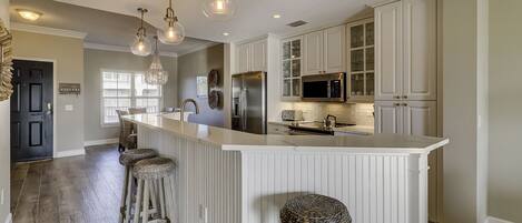 A modern kitchen with a central island, bar stools, stainless steel appliances, and pendant lighting.
