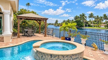 A swimming pool with a hot tub, outdoor seating, and a view of the water.