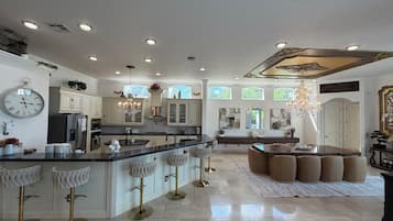 A spacious kitchen with a central island, bar stools, and a dining area with a chandelier.