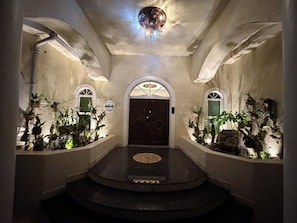 Un couloir doté d’un plancher sombre, d’arcades au niveau des portes et de plantes en pot disposées le long des murs.