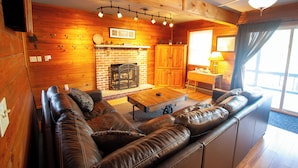 A cozy log cabin interior with a leather sofa, a fireplace, wooden walls, and a ceiling fan.