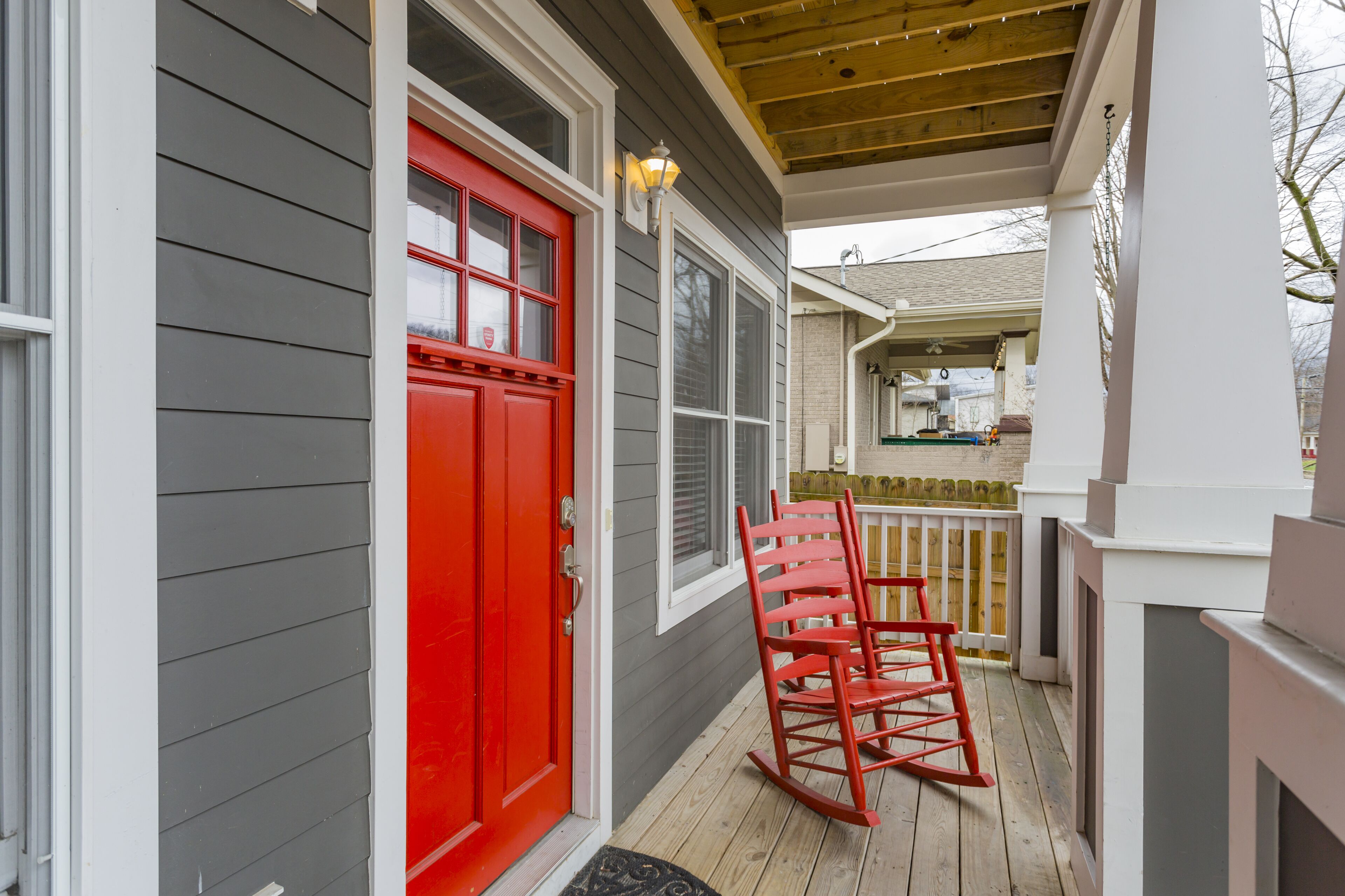 Une véranda avec une porte rouge, une chaise berçante et une terrasse en bois.