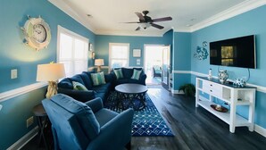 Un salon avec un canapé bleu, une table basse ronde et un téléviseur fixé au mur.