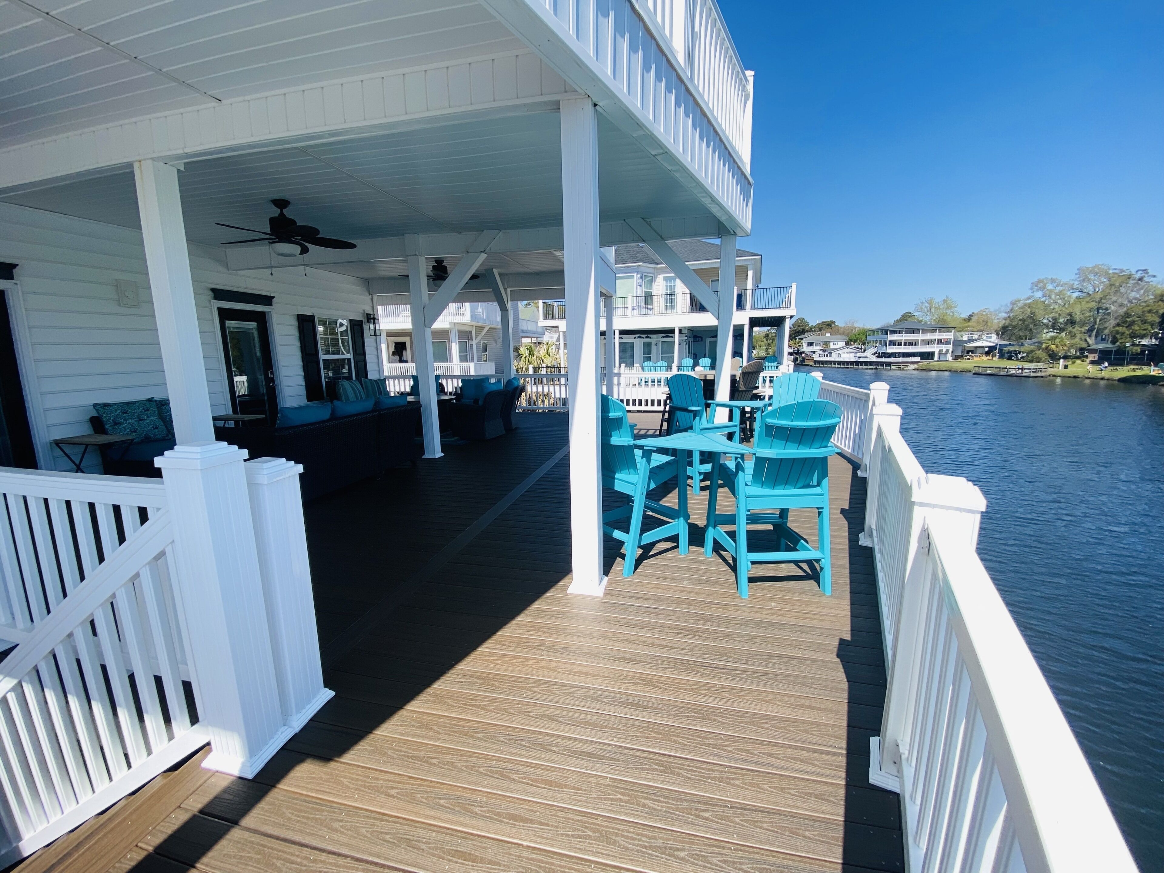 A wooden deck with outdoor seating and a white railing overlooking a body of water.