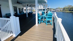 Une terrasse en bois avec des sièges extérieurs et une balustrade blanche donnant sur une étendue d’eau.