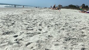 Une plage de sable avec des empreintes de pas, quelques personnes et des parasols de plage.