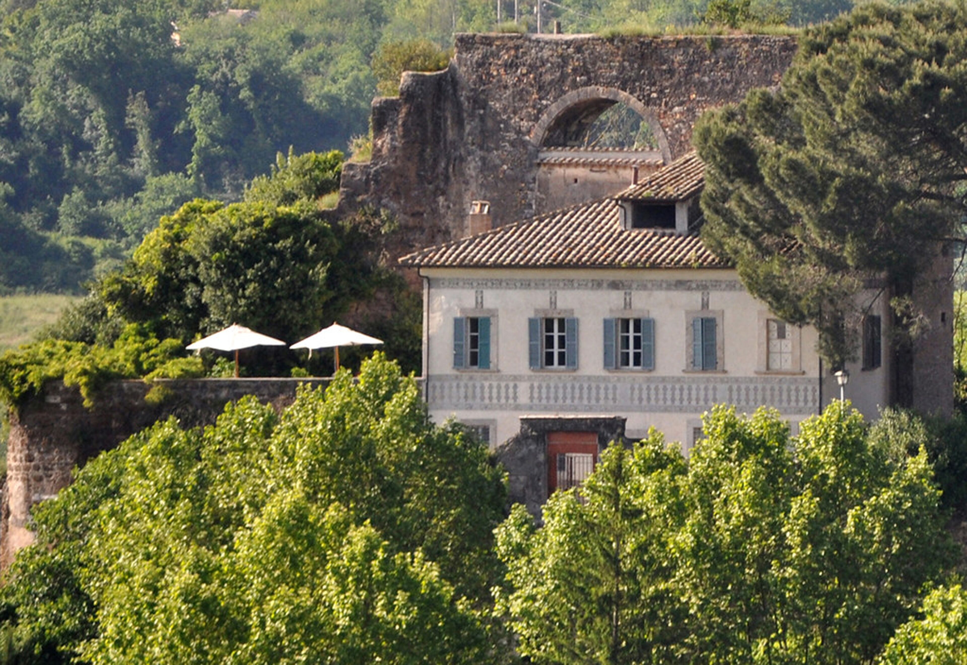 A historic building with a balcony, surrounded by lush greenery and a stone wall.