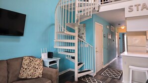 Ein Wohnzimmer mit braunem Sofa, einer weißen Wendeltreppe und einem flachbildschirmfernseher an der Wand.