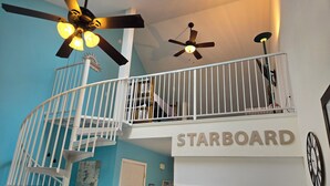 Eine zweistöckige Wohnung mit Wendeltreppe, Deckenventilator, Küche mit Kühlschrank und Herd sowie einem Schild mit der Aufschrift 'STARBOARD'.