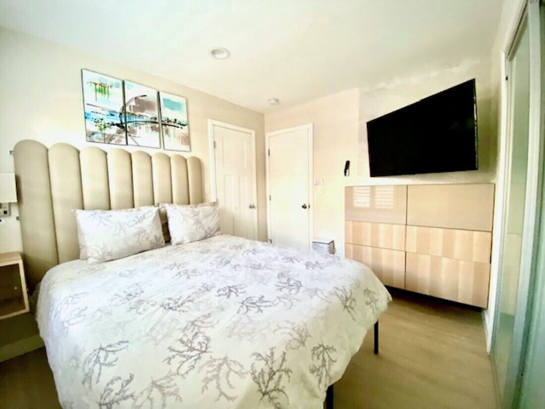 A bedroom with a large bed, a television mounted on the wall, and a door leading to another room.