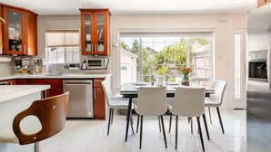 A modern kitchen with white cabinetry, a dining area with four chairs, and a large window offering a view of greenery outside.