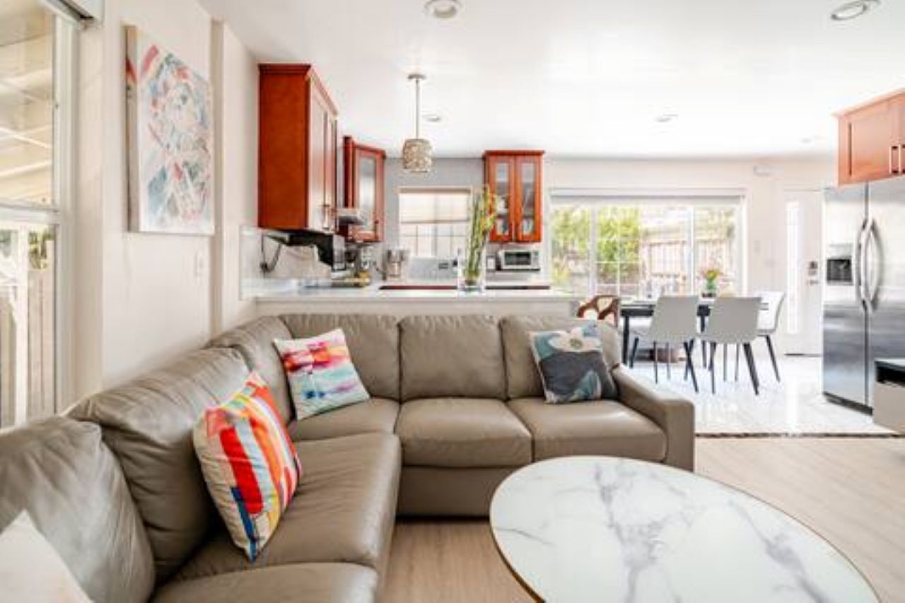 A modern living room with a sectional sofa, a marble coffee table, and a kitchen in the background.