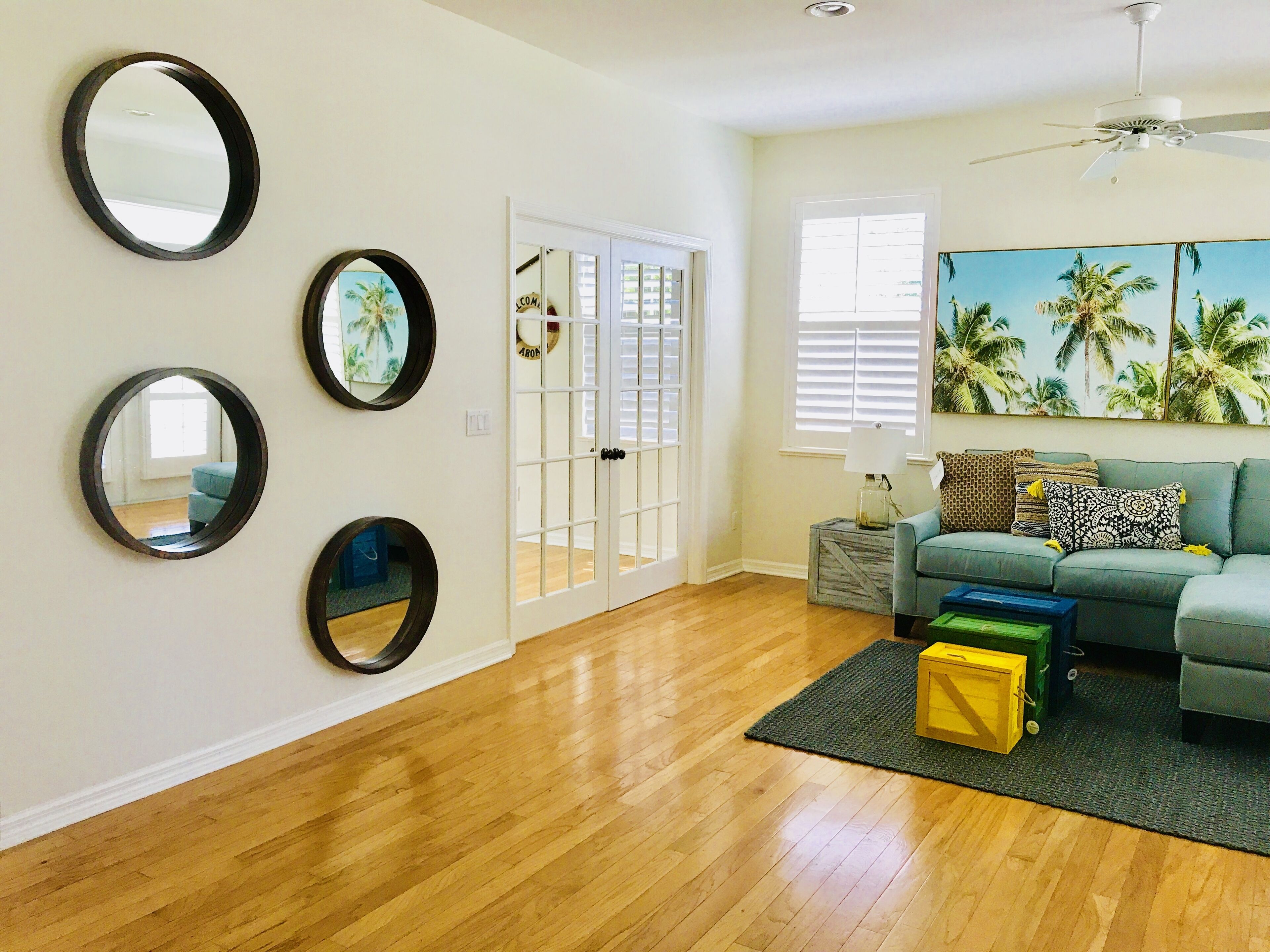 A living room with a wooden floor, a green sofa, and a painting of palm trees.