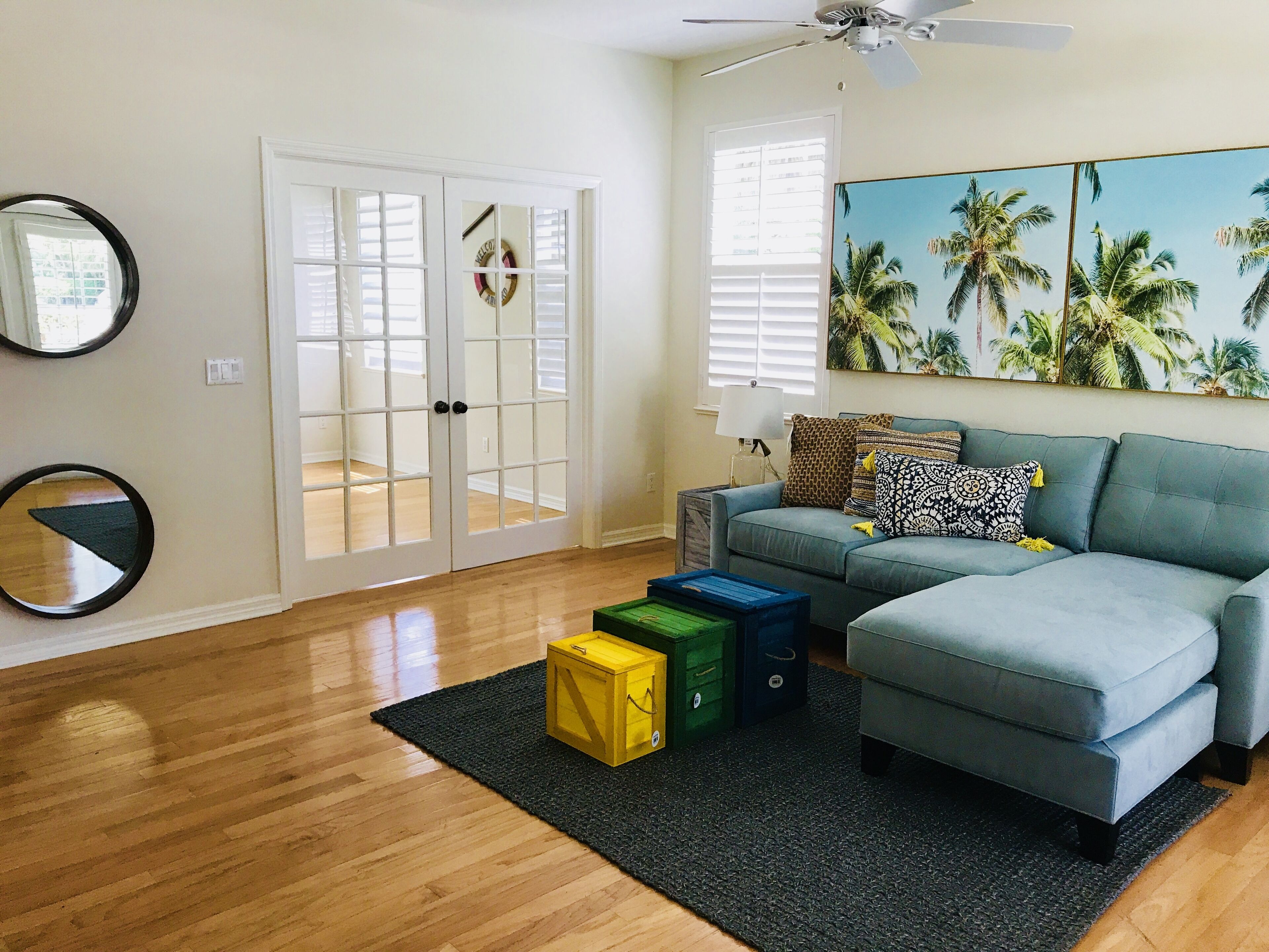 A living room with a grey sectional sofa, a black rug, and a painting of palm trees.