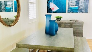 Un comedor con una mesa de madera, bancos, una jarra azul y una lámpara colgante.
