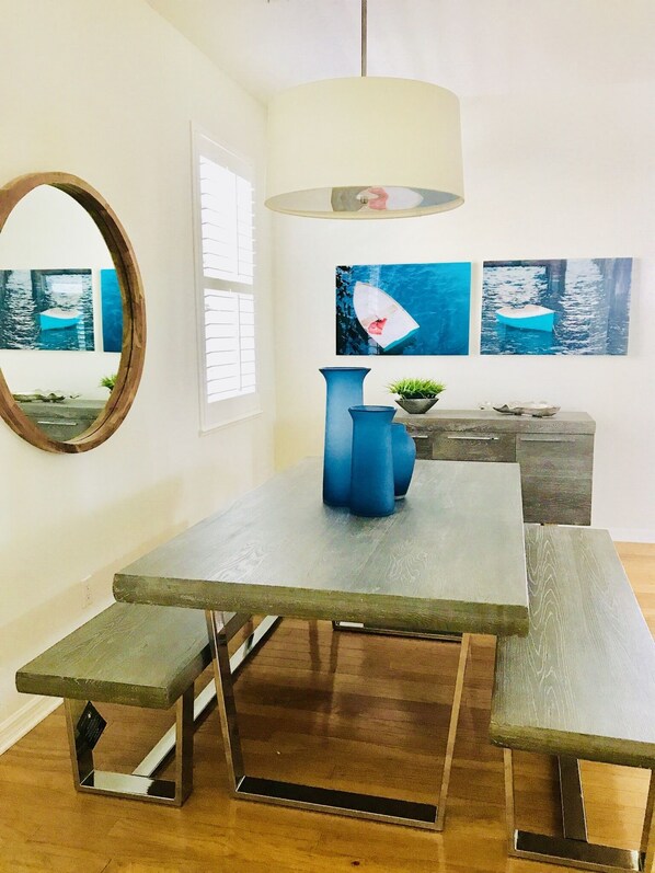 A dining area with a wooden table, benches, a blue pitcher, and a hanging light fixture.