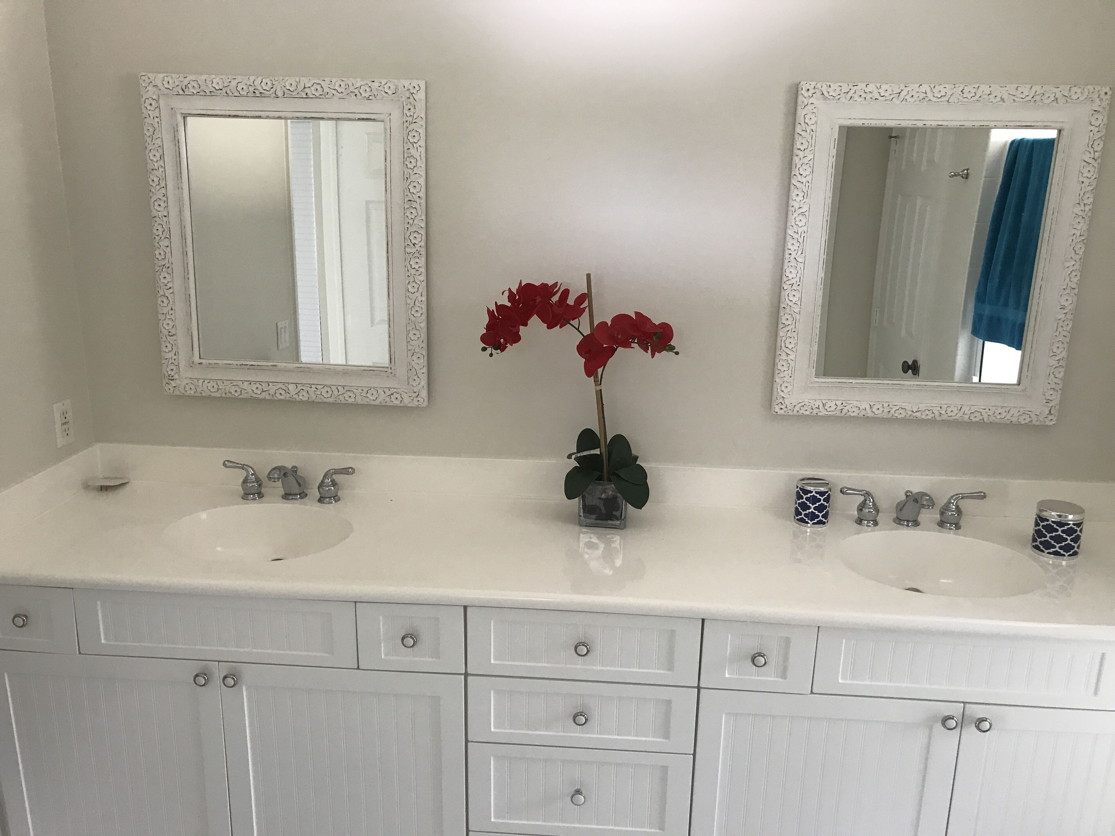A bathroom with two sinks, two mirrors, and a vase with red flowers.