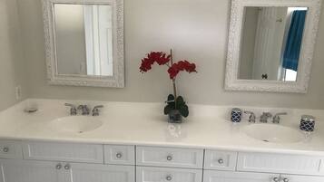 A bathroom with two sinks, two mirrors, and a vase with red flowers.