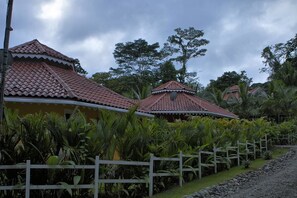 Uma fileira de edifícios em estilo tradicional, com telhados de terracota, cercada por vegetação exuberante e um muro branco.