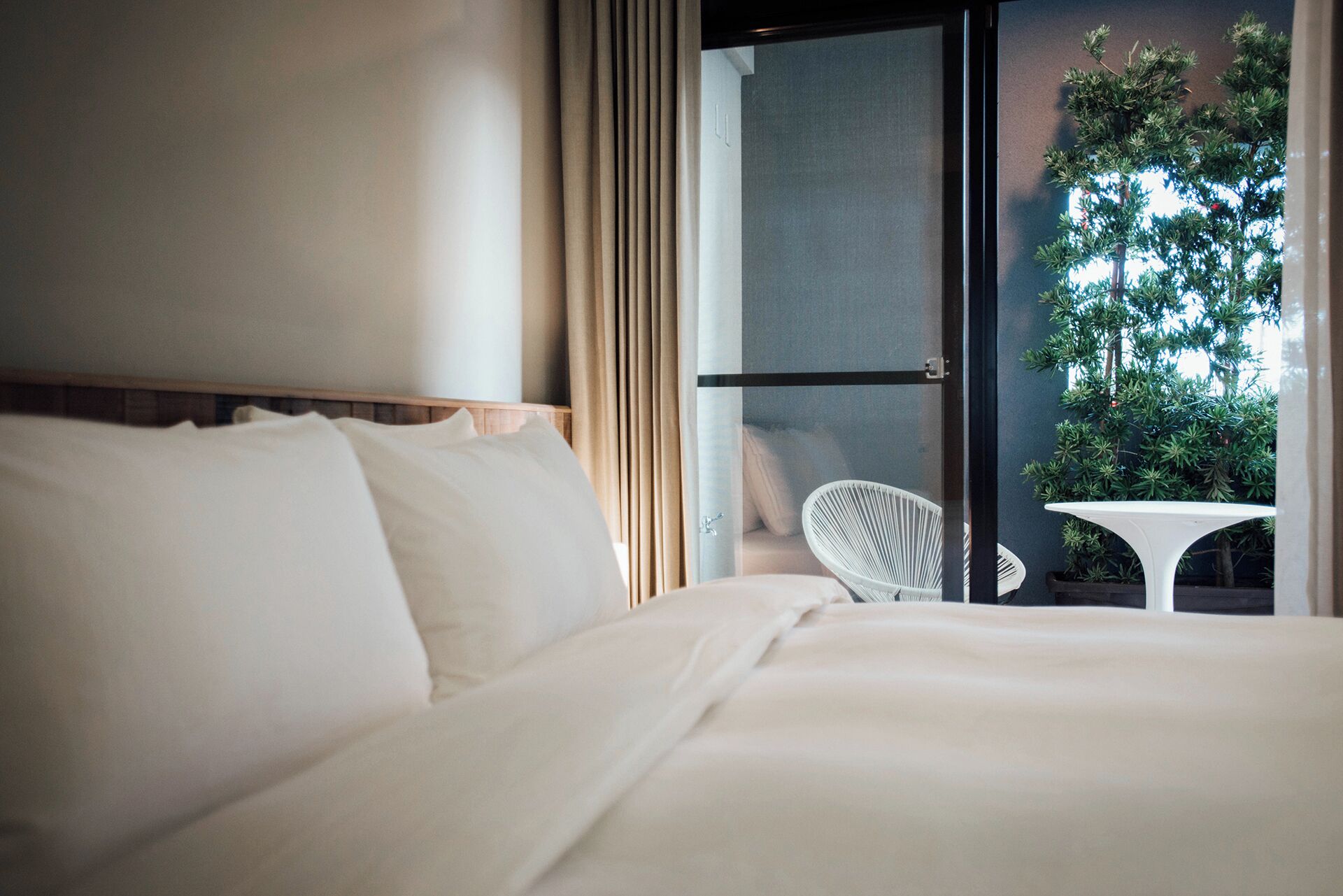 A hotel room with a bed, a chair, and a view of a balcony with a plant.