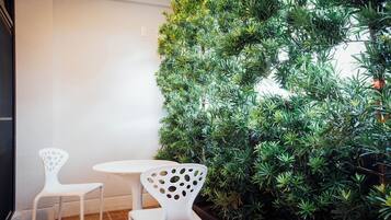 Un pequeño espacio al aire libre con dos sillas blancas y una mesa, rodeado por un seto verde frondoso.