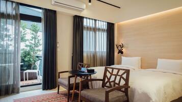 Habitación de hotel con cama, escritorio y silla, una mesita y vistas al exterior a través de una puerta corredera.