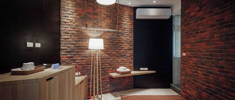A modern bathroom with a brick wall, a wooden vanity, a floor lamp, and a patterned rug.