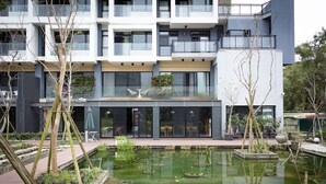 A modern building with a courtyard featuring a pond, surrounded by trees and plants.