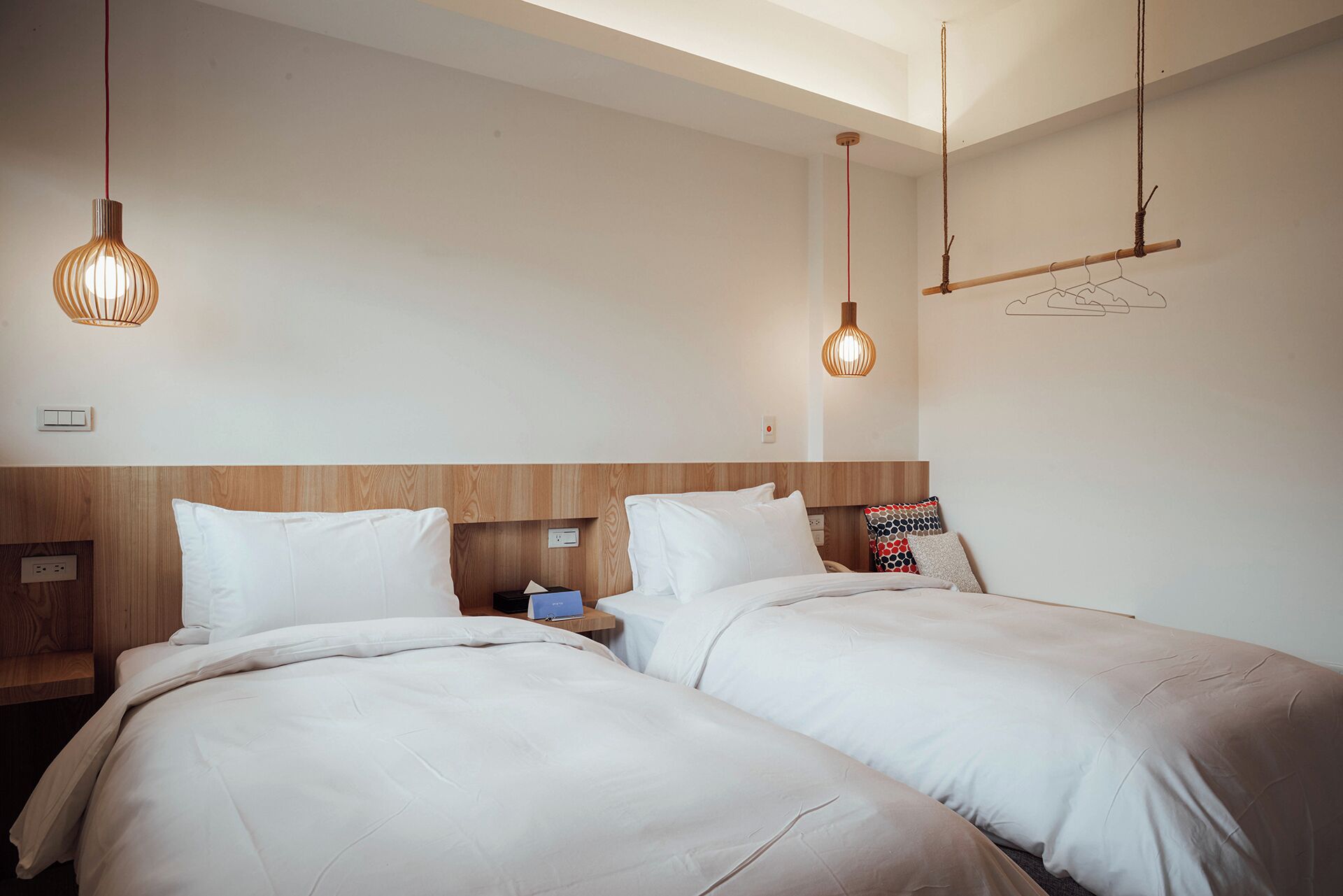 Une chambre d’hôtel avec deux lits, des têtes de lit en bois, des tables de chevet et des lampes suspendues.