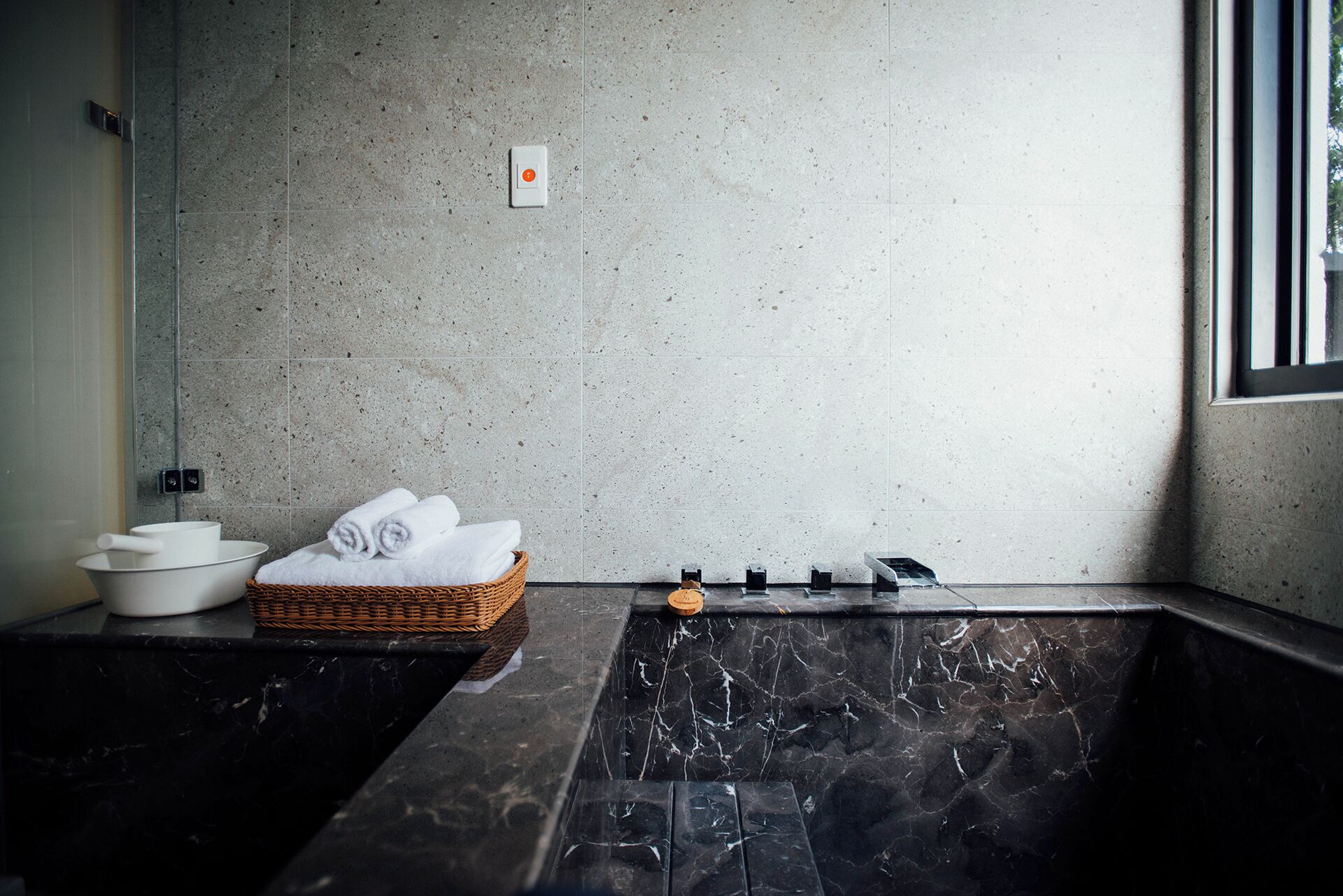 Un baño moderno con un lavabo de mármol, una cesta de mimbre con toallas y una zona de ducha.