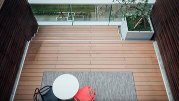 Een houten terras met een tafel, stoelen en een glazen balustrade, met uitzicht op een tuin.