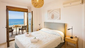 A bedroom with a bed, bedside table, lamp, and a view of the sea through an open door. - Irida beachfront Villa for 12 next to all amenities (Rethymno)