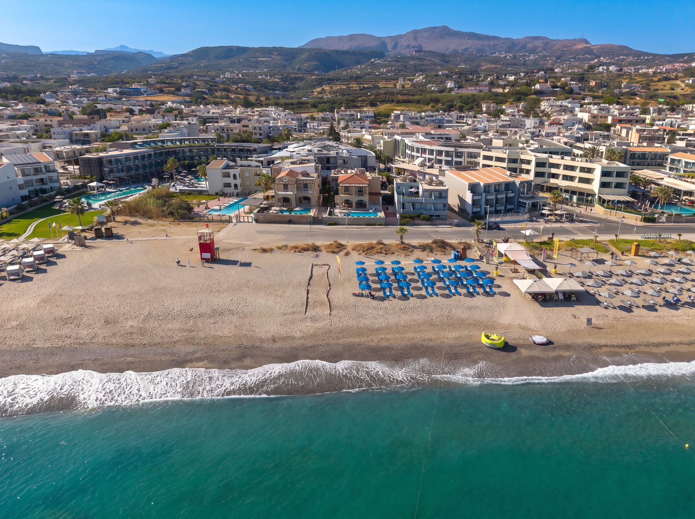 A coastal resort with multiple buildings, a beach with umbrellas, and a clear view of the sea.