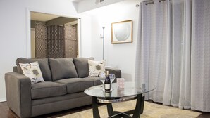 Un salon avec un canapé gris, une table basse en verre et un tapis à motifs.