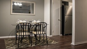 Un coin repas avec une table dressée pour deux personnes, un miroir au-dessus de la table et un réfrigérateur dans la pièce adjacente.