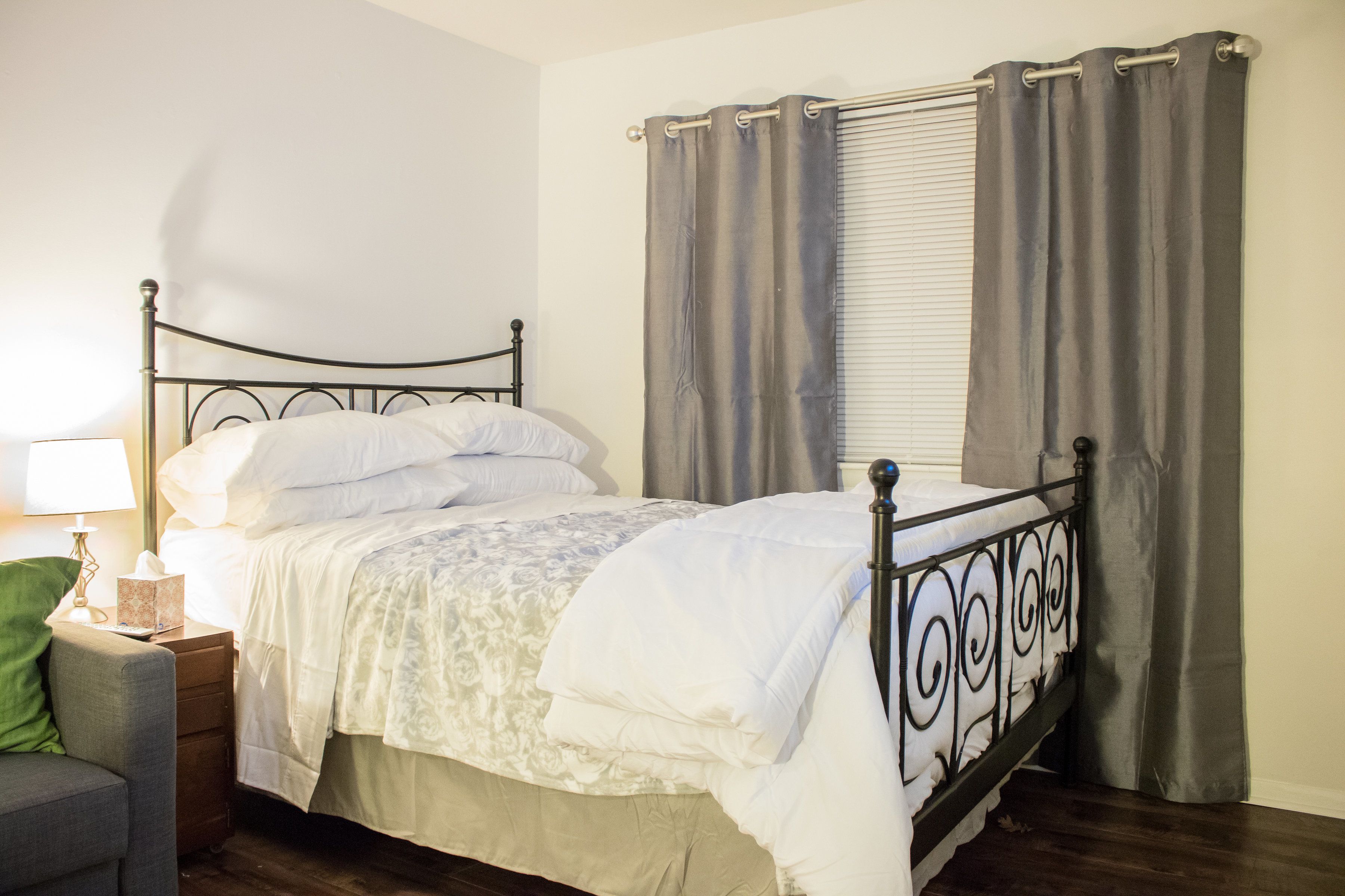 A neatly made bed with a metal frame, a bedside table with a lamp, and a chair.