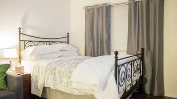 A neatly made bed with a metal frame, a bedside table with a lamp, and a chair.