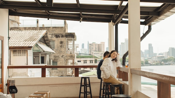 A rooftop bar with a city view, wooden tables, and a railing. - Hostel Urby (Bangkok)