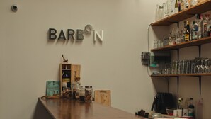 A bar area with a wooden counter, shelves with bottles, and a sign that reads "BARBON". - Hostel Urby (Bangkok)