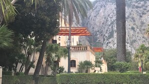 A building with a red roof, surrounded by palm trees and a mountainous backdrop.